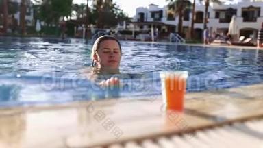 女人游泳到游泳池的边缘，取新鲜的果汁，喝它，然后游泳离开，阳光明媚的一天在游泳池里。